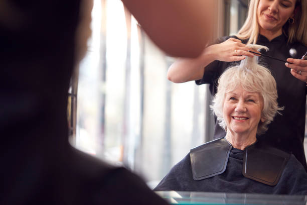 Elderly woman smiling in a salon while getting her hair styled by a professional hairstylist