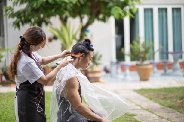 Hairdresser providing outdoor haircut to male client in garden setting.