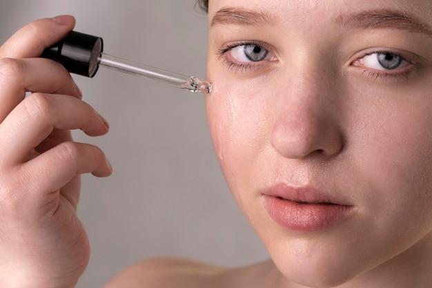 Close-up of a young woman applying serum to face with dropper, focusing on skincare and beauty