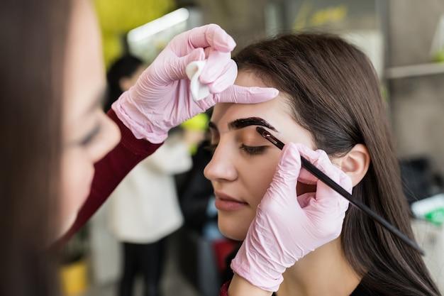 A beautician applying eyebrow makeup to a female client in a salon