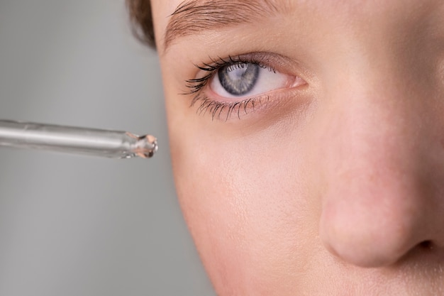 A close-up image of a person's eye with a dropper applying liquid near it. The focus is on the eye and the tip of the dropper, demonstrating precision in application.