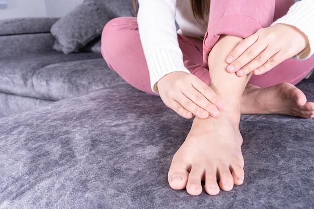 Woman examining her foot while sitting on a gray couch.